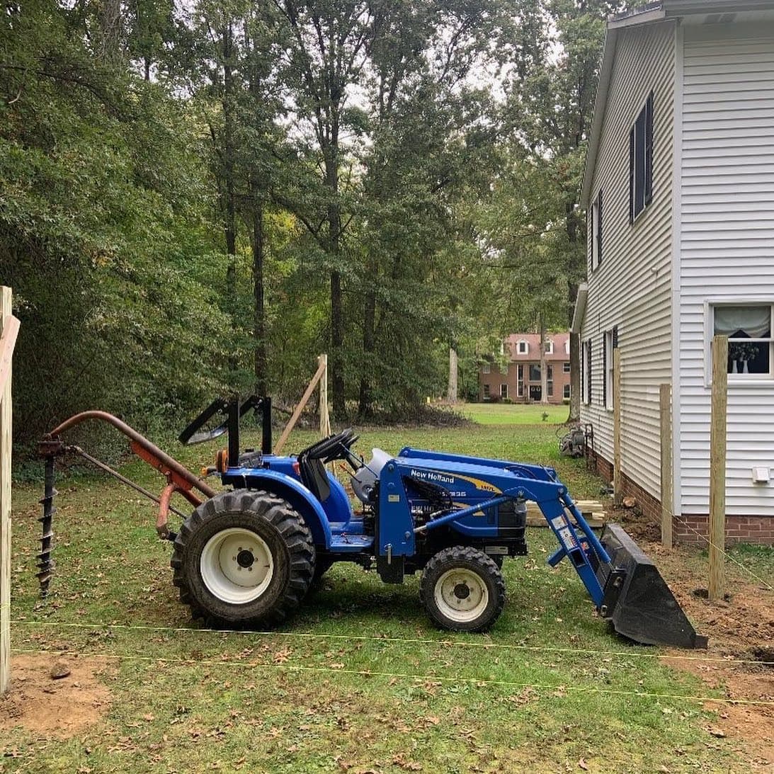 Compact tractor with front loader and post-hole auger at a job site